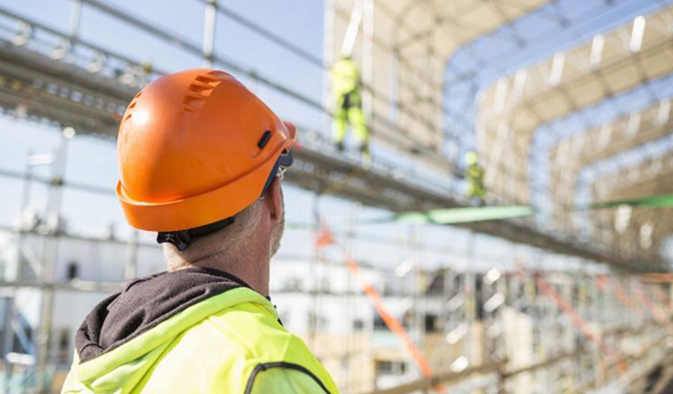 Worker with protective gear looking up at construction site.