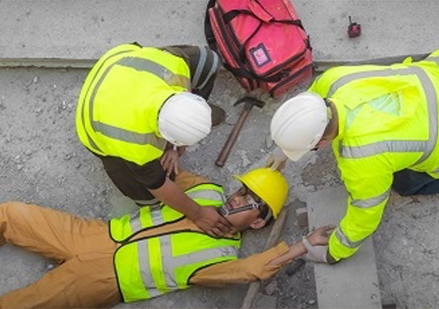 Injured worker lays unconscious while two workers clad in personal protective equipment kneel over in concern.