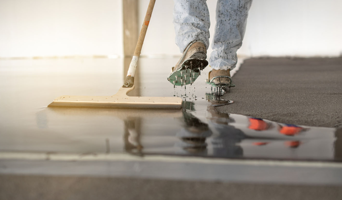 Worker cleaning a walking-working surface, with a mop, his foot hovers over a pool of water, dripping wet. This is a slip hazard.